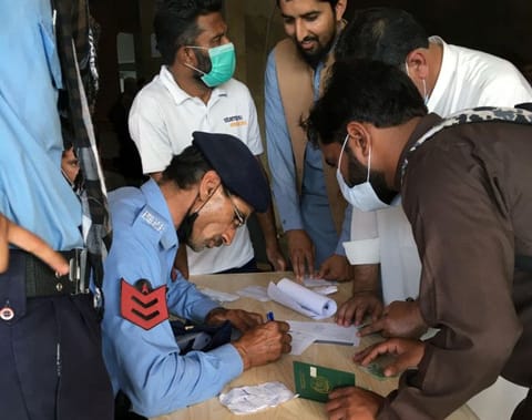 A police officer helps men to fill out forms to obtain a vaccine at a centre in Islamabad, Pakistan on June 28, 2021. 