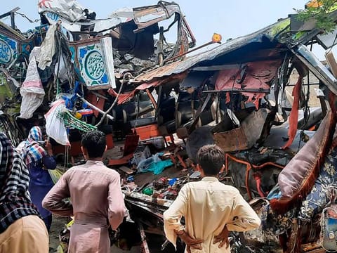Local residents look at the wreckage of a bus at the site of an accident near Dera Ghazi Khan, Pakistan, Monday, July 19, 2021.