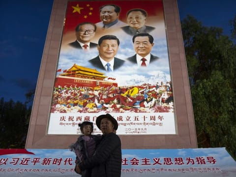 A man holds a girl as they pose for a photo in front of a large mural depicting Chinese President Xi Jinping, bottom centre, and other Chinese leaders at a public square at the base of the Potala Palace in Lhasa in western China's Tibet Autonomous Region on June 1, 2021. Chinese leader Xi Jinping has made a rare visit to Tibet. 