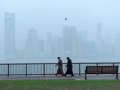 Residents take a walk on a cold foggy morning at Buheirah corniche in Sharjah. 