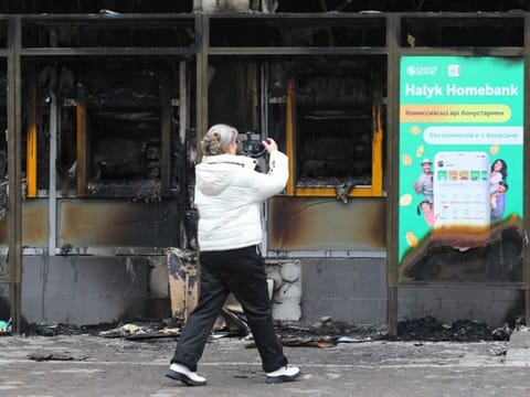 A woman films a building, which was burnt during mass protests triggered by fuel price increase, in Almaty, Kazakhstan January 9, 2022. 
