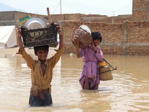 Children carrying household items wade through a flooded area after a monsoon rainfall in Quetta on July 5, 2022. 