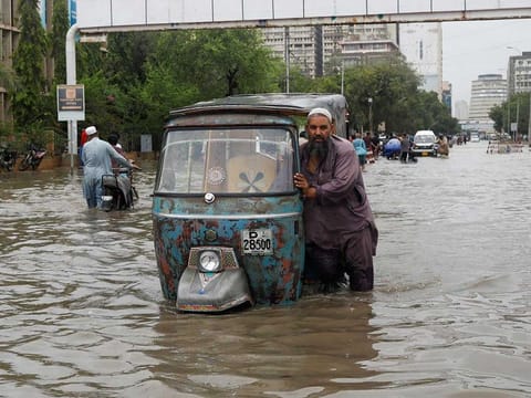 A man pushes his rickshaw (tuk tuk) through a flooded road during the monsoon season in Karachi, Pakistan July 9, 2022. 