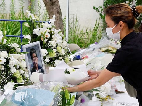 A woman offers flowers as people mourn for late former Japanese Prime Minister Shinzo Abe, who was shot while campaigning for a parliamentary election, at Headquarters of the Japanese Liberal Democratic Party in Tokyo, Japan July 12, 2022. 