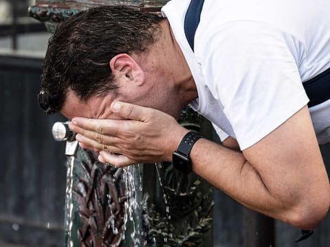 A man cools his face with water from a fountain in Paris on July 13, 2022. 