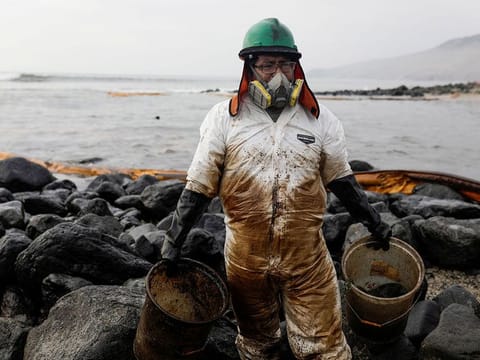 FILE PHOTO: A worker cleans up an oil spill at the beach as demonstrators take part in a protest outside Repsol's La Pampilla refinery against the recent oil spill that has caused an ecological disaster on the coasts of Lima, in Ventanilla, Peru January 29, 2022.