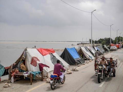Motorists ride past temporary tents set up for displaced people who fled their flood hit homes following heavy monsoon rainfalls in Sukkur of Sindh province, southern Pakistan on August 26, 2022.