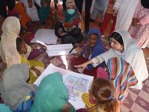 This handout picture taken and released by Chief Minister House Office of Sindh Province on October 12, 2022 shows Yousafzai (right) speaking with flood-affected children at a makeshift school in Johi, Dadu district of Sindh province.  
