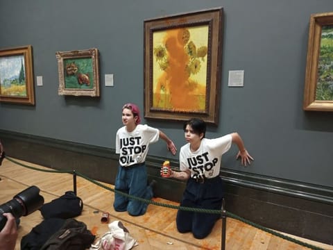 Handout photo issued by Just Stop Oil of two protesters who have thrown tinned soup at Vincent Van Gogh's famous 1888 work Sunflowers at the National Gallery in London, on October 14, 2022.  