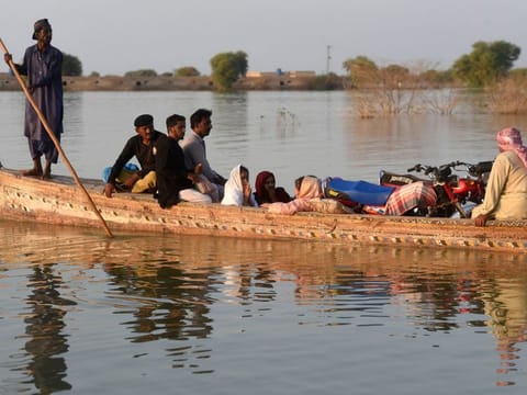 Internally displaced people use a boat to cross a flooded area at Dadu in Sindh province on October 27, 2022.  