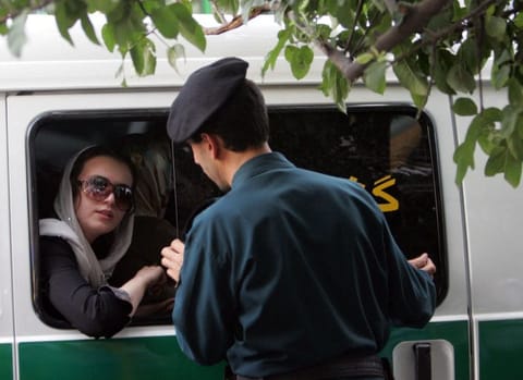 An Iranian policeman speaks with a woman sitting in a police car after she was arrested because of her "inappropriate" clothes during a crackdown to enforce Islamic dress code in the capital Tehran.  