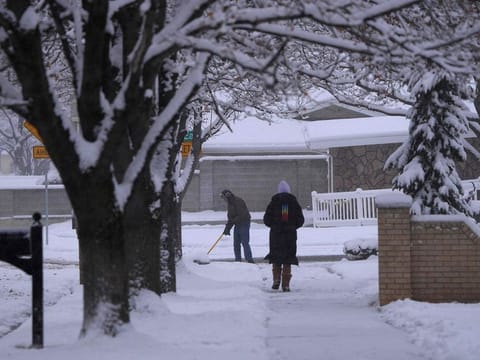  A man clears his driveway of snow as a woman walks down the sidewalk after an overnight storm in Provo,Utah on December 13,  2022.