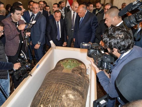 Egypt's Foreign Minister Sameh Shoukry (C-R) and the head of the Supreme Council of Antiquities Mostafa Waziri (C-L) are surrounded by journalists as they inspect an ancient Egyptian wooden sarcophagus being handed over and which was formerly displayed at Houston Museum of Natural Sciences after having been looted and smuggled years prior, at the foreign ministry headquarters in the capital Cairo on January 2, 2023.