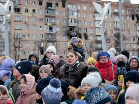Local citizens watch a performance near a Christmas tree decorated for Orthodox Christmas and the New Year festivities in Mariupol, in Donetsk region, eastern Ukraine, on January 5, 2023.  