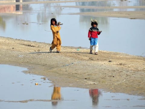 Internally displaced flood-affected girls walk beside the flood waters near a makeshift camp in the flood-hit area of Dera Allah Yar in Jaffarabad district of Balochistan province on January 9, 2023.  