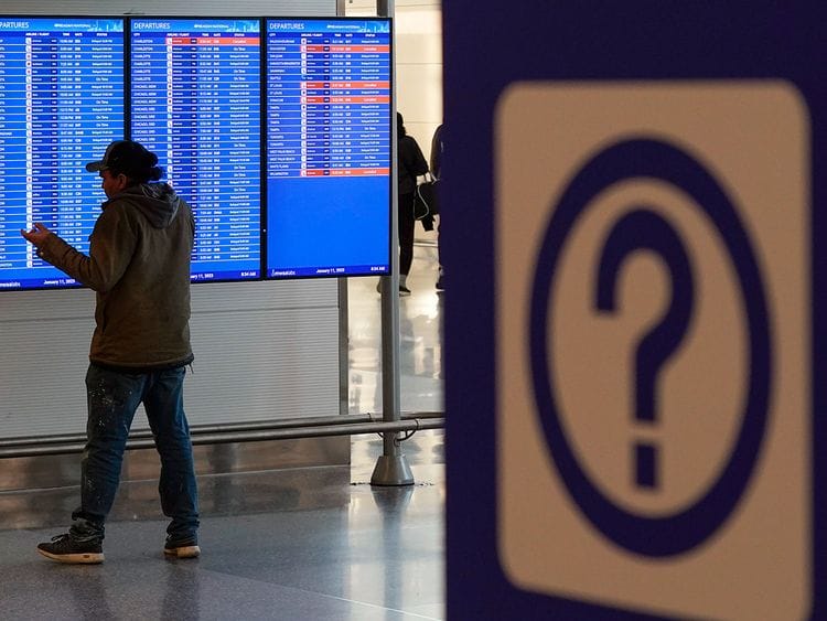 A person talks on a mobile phone by a video board showing flight delays and cancellations at Ronald Reagan Washington National Airport in Arlington, Virginia, on January 11, 2023. 