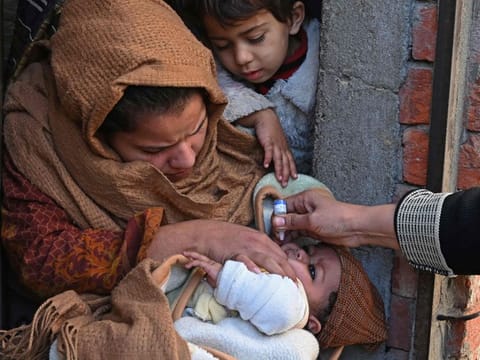A health worker administers polio vaccine drops to a child during a vaccination campaign in Lahore on January 16, 2023. (Photo by Arif ALI / AFP)