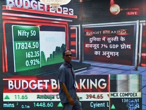 A staff worker walks past a digital display showing India's Finance minister Nirmala Sitharaman presenting the union budget in the Parliament, at Bombay Stock Exchange (BSE) in Mumbai on February 1, 2023. 