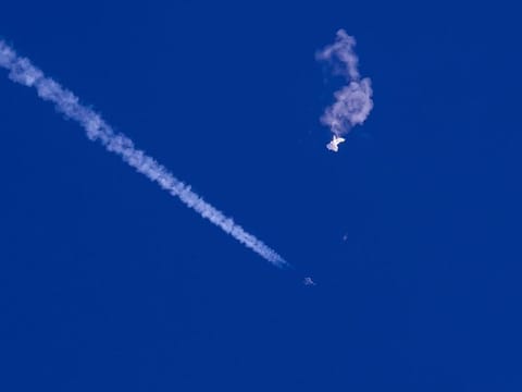 In this photo provided by Chad Fish, the remnants of a large balloon drift above the Atlantic Ocean, just off the coast of South Carolina, with a fighter jet and its contrail seen below it, Saturday, Feb. 4, 2023. 