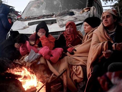 People sit near a bonfire amidst the rubble of collapsed buildings in Kahramanmaras, on February 8, 2023, two days after a 7,8-magnitude earthquake struck southeast Turkey
