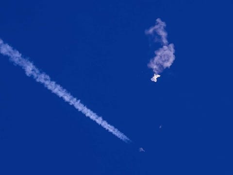 In this photo provided by Chad Fish, the remnants of a large balloon drift above the Atlantic Ocean, just off the coast of South Carolina, with a fighter jet and its contrail seen below it, Feb. 4, 2023.  