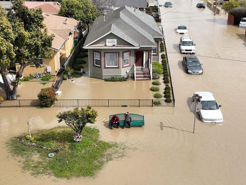 An aerial view shows people sitting on a bench in a flooded neighborhood in the unincorporated community of Pajaro in Watsonville, California on March 11, 2023.