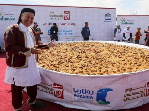 People gather around a giant couscous prepared by Libyan chefs on the site of the ancient Roman theatre of Sabratha, about 70 km west of the capital Tripoli, ,on March 10, 2023.