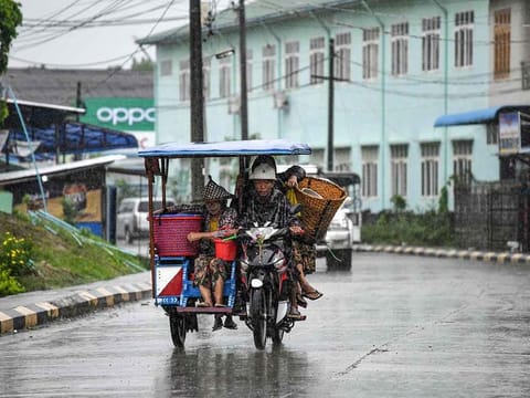 People ride a sidecar motorcycle in an almost empty street in Kyauktaw in Myanmar’s Rakhine state on May 14, 2023, ahead of the expected landfall of Cyclone Mocha. 