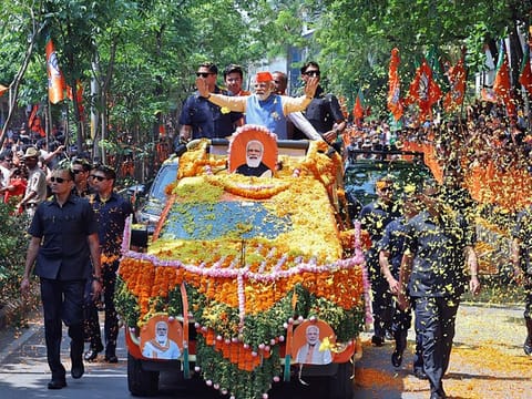 Prime Minister Narendra Modi waves while being showered with flower petals by the supporters during a roadshow for the Karnataka Assembly elections, in Bengaluru 