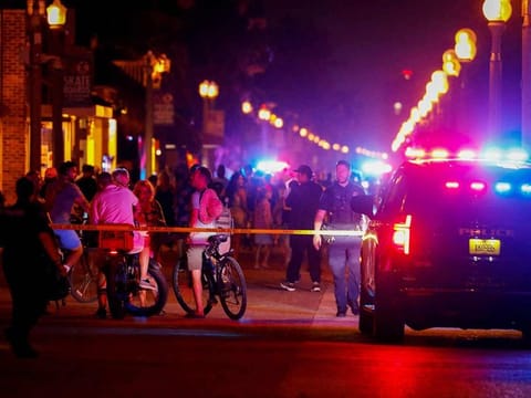 Beachgoers are seen next to law enforcement officers on a crime scene as they respond to a shooting at Hollywood Beach, Florida.   