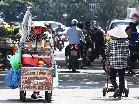 Street vendor Vu Thi Phuong (L) pushes her trolley to sell coffee and soft drinks in Hanoi on June 1, 2023. The north of Vietnam has been struck by heatwaves in recent weeks. 
