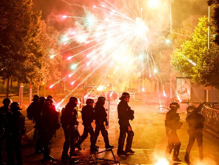 French police stand in position as fireworks go off during clashes with youth