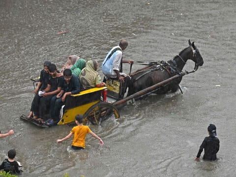 People ride on a horsecart through a flooded street after heavy rainfall in Lahore on July 5, 2023.  