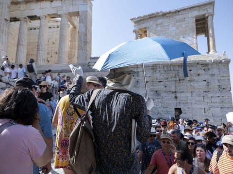 A tour guide uses an umbrella and gloves to shield himself from the sun with while touring the Acropolis archaeological site, during extreme hot weather conditions, in Athens, Greece, on July 14, 2023.  