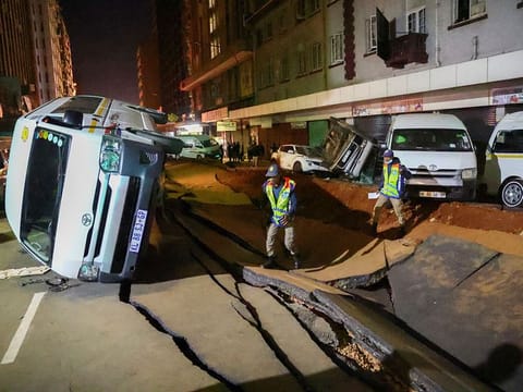 Police officers inspect damaged cars and the road after a suspected gas explosion injured several people and caused significant damage, in the central business district of Johannesburg, on July 19, 2023. 