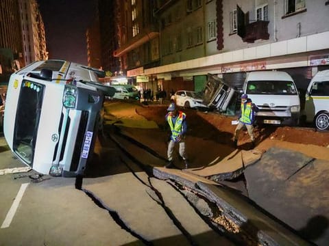 Police officers inspect damaged cars and the road after a suspected gas explosion injured several people and caused significant damage, in the central business district of Johannesburg, on July 19, 2023. 