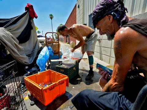 Charles Sanders, 59, right, pauses as Kevin Hendershot, 47, pours ice into a bucket outside their tent in "The Zone" homeless encampment, in downtown Phoenix.  
