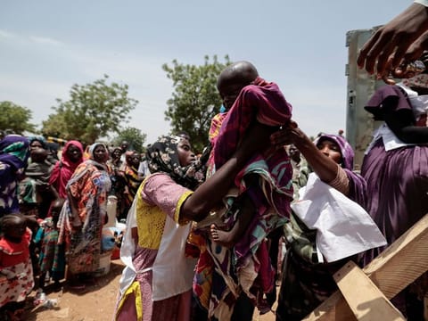 Red Cross workers help a Sudanese child who fled the conflict in Geneina in Sudan's Darfur region with his family, to get on a truck that will relocate them from a school where they were temporarily accommodated to a refugee camp in Adre, Chad, on July 23, 2023. 