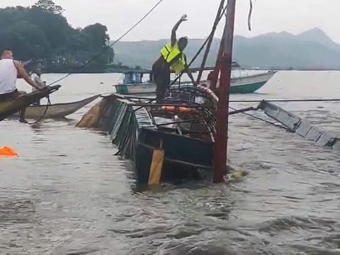 In this image from video provided by the Philippine Coast Guard, a man stands on a capsized passenger boat as they undergo rescue operations at Binangonan, Rizal province, east of Manila, Philippines on Thursday July 27, 2023.  