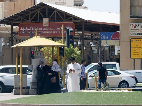 People take shelter from the sun under a traffic light in Kuwait City amidst a heatwave. 