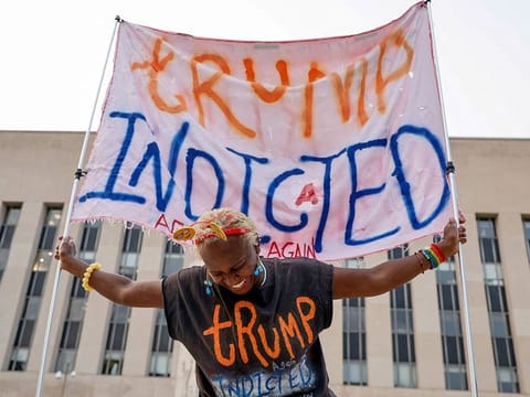 A woman holds a banner in front of the federal courthouse where former US President and Republican presidential candidate Donald Trump is expected later this week to answer charges after a grand jury returned an indictment of Trump in the special counsel's investigation of efforts to overturn his 2020 election defeat in Washington, on August 1, 2023. 