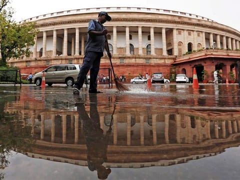 File photo: Indian parliament building is reflected in a puddle after the rain as a man sweeps the water in New Delhi. India has been trying to push local manufacturing by giving production-linked incentives in over two dozen sectors, including electronics. 