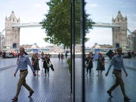 File photo: People reflected in a building glass, walk on the Southbank of the River Thames, with London Bridge on the background, central London.  