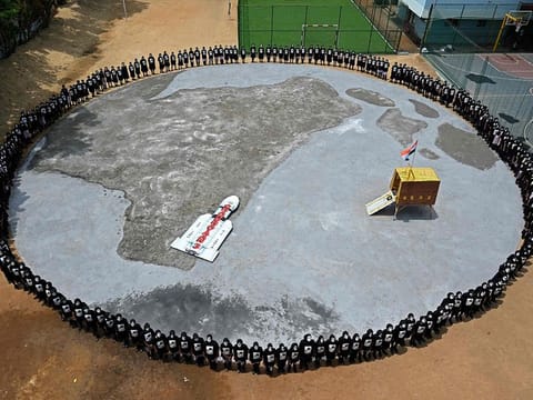 Students with painted faces form a circle around a replica of the Chandrayaan-3 spacecraft in Chennai on August 22, 2023. 