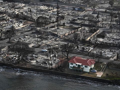 An aerial image shows a red roofed house that survived the fires surrounded by destroyed homes and buildings burned to the ground in the historic Lahaina in the aftermath of wildfires in western Maui in Lahaina, Hawaii on August 10, 2023. Embattled officials in Hawaii who have been criticized for the lack of warnings as a deadly wildfire ripped through a town insisted on August 16 that sounding emergency sirens would not have saved lives. At least 110 people died when the inferno levelled Lahaina last week on the island of Maui, with some residents not aware their town was at risk until they saw flames for themselves. 
