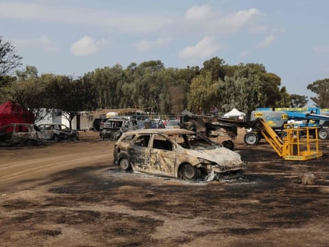 An Israeli soldier walks past burnt vehicles at the site of the weekend attack on the Supernova desert music Festival by Palestinian militants near Kibbutz Reim in the Negev desert in southern Israel on October 10, 2023.  