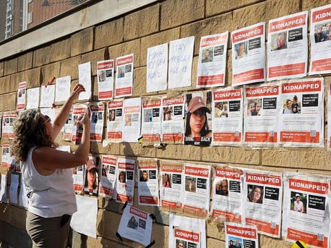 Supporters and family members of Israeli hostages snatched by the militant group Hamas, plaster their images on a wall during a rally outside of the Israeli military base of HaKirya in central Tel Aviv on October 14, 2023. 