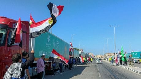 People with Egyptian flags cheer next to a convoy of trucks carrying humanitarian aid to Palestinians by Egyptian NGOs, as they wait for an agreement on the Rafah border crossing to enter Gaza, amid the ongoing conflict between Israel and the Palestinian Islamist group Hamas, in the city of Al Arish in Egypt's Sinai peninsula, Egypt, October 15, 2023.  