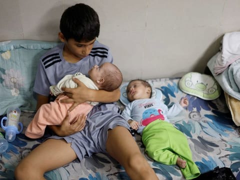 A displaced Palestinian boy, who fled with his family from their house amid Israeli strikes, looks after his twin siblings as they take shelter at Nasser hospital in Khan Younis in the southern Gaza Strip October 29, 2023.  