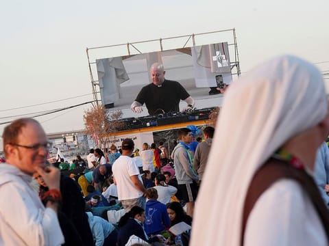 Roman Catholic priest Guilherme Peixoto, on video screen, plays techno music to help pilgrims wake up at Parque Tejo in Lisbon on Sunday, Aug. 6, 2023, where Pope Francis will preside over a mass celebrating the 37th World Youth Day later in the day.